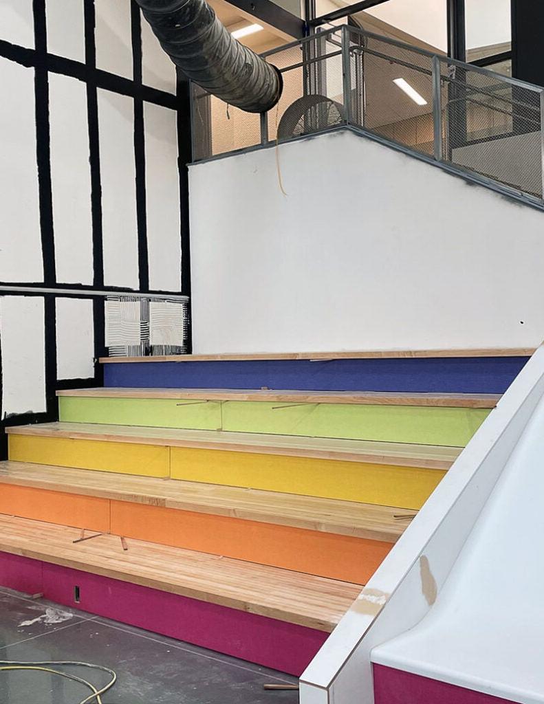 wide and deep stairs have wood tops and colored risers. From top risers are blue, green, yellow, orange, and bright pink